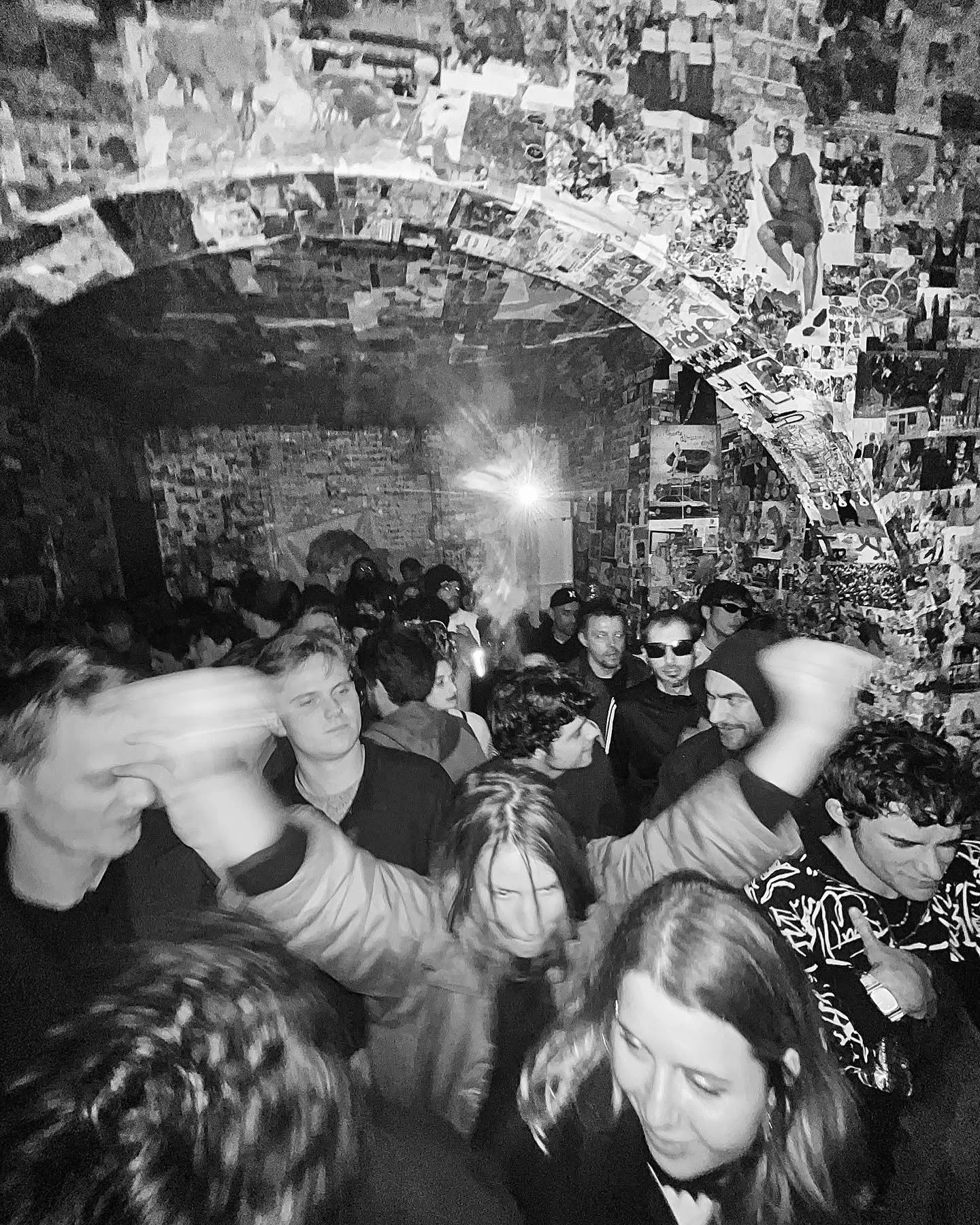 Crowd dancing in a vaulted passage covered in posters